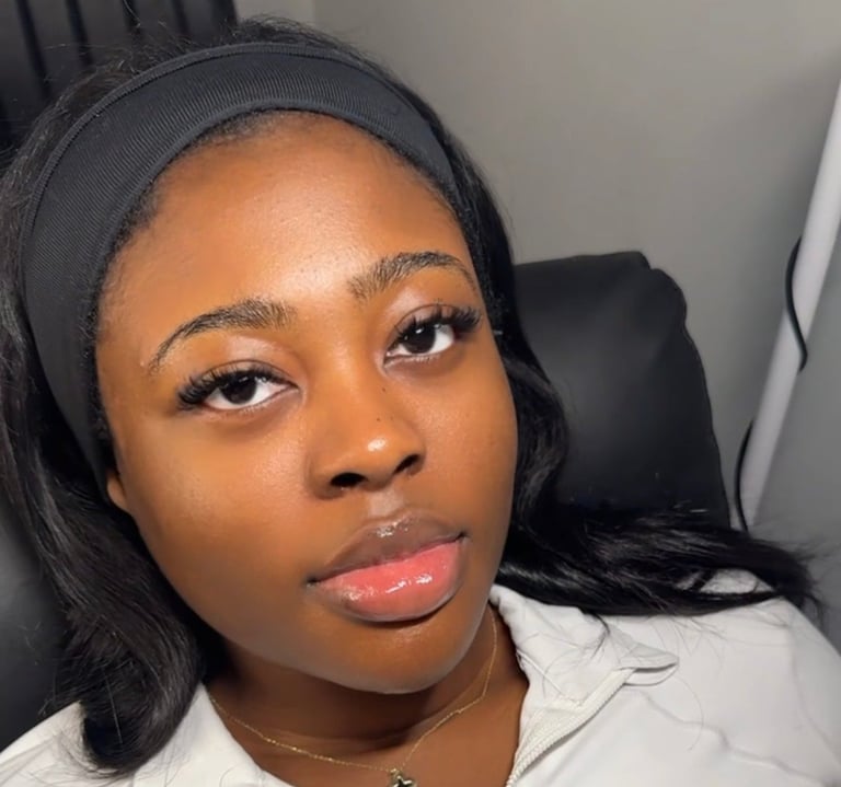 Close-up selfie of a woman wearing a gray headband and white top, seated indoors with a neutral expression