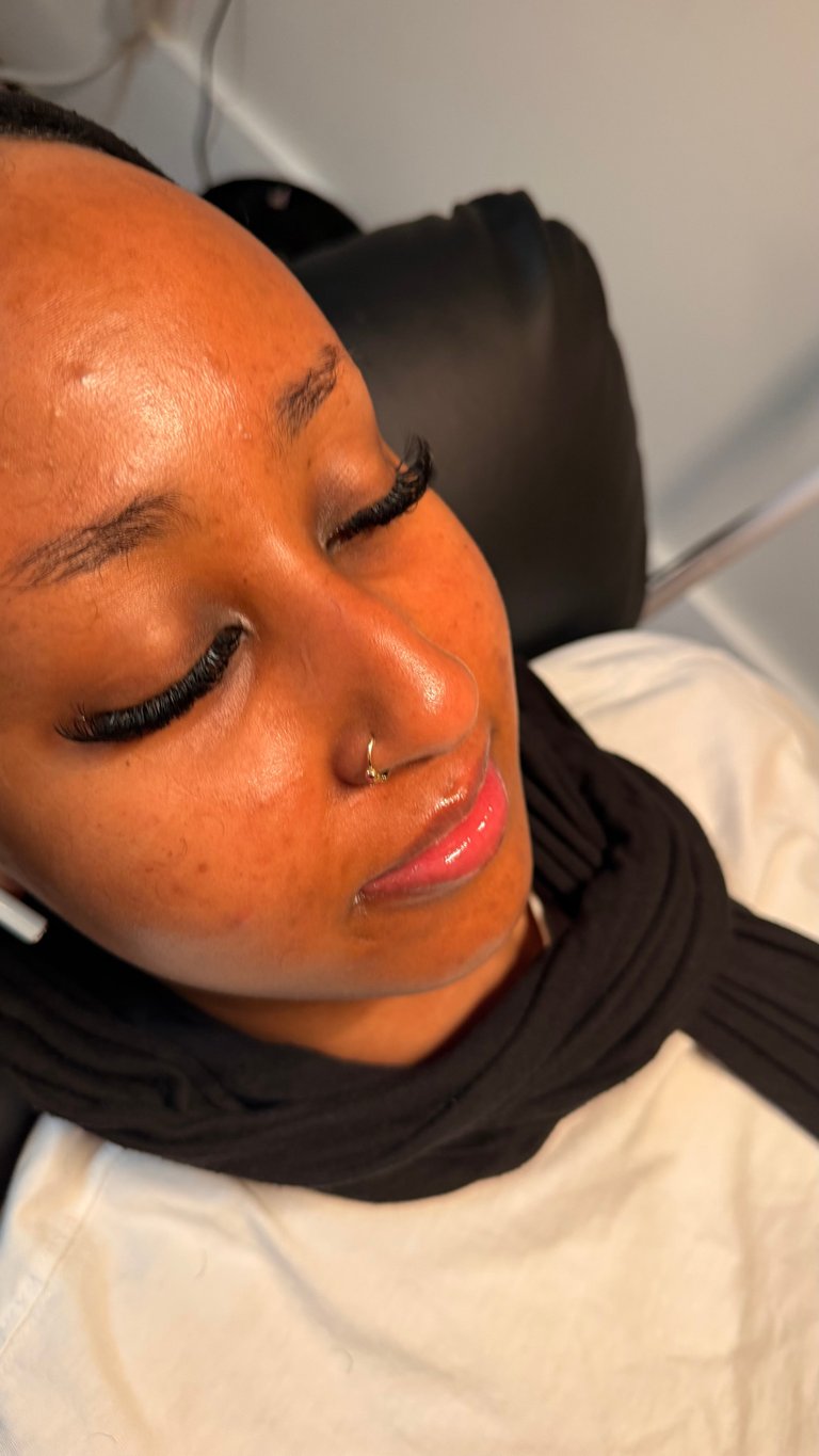 Close-up portrait of person with orange skin tone, dramatic eye makeup, pink lips, and nose piercing, wearing black and white clothing