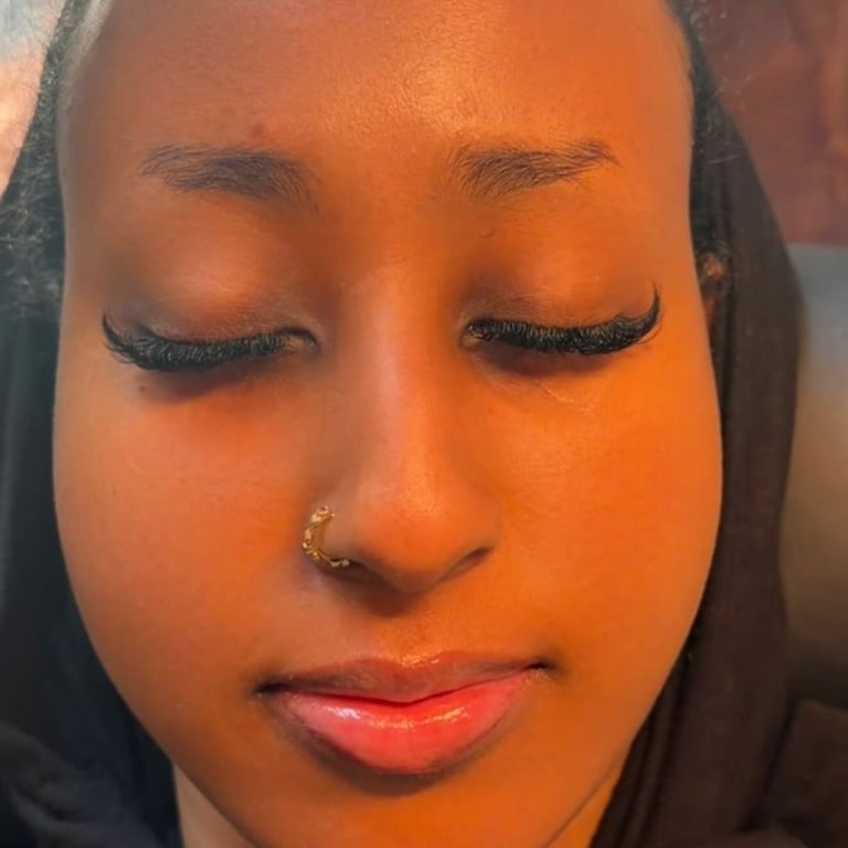 Close-up portrait of a person with closed eyes, full lips, nose ring, and dark hair against an orange-toned background